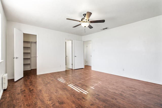 unfurnished bedroom featuring a spacious closet, visible vents, baseboards, wood finished floors, and a ceiling fan