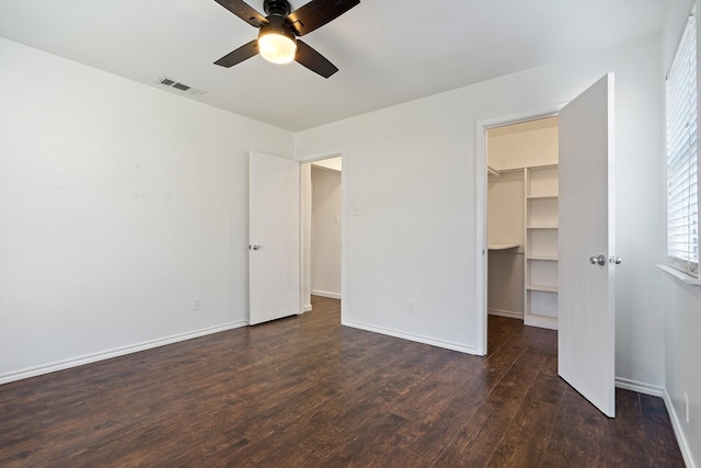 unfurnished bedroom with baseboards, visible vents, dark wood-type flooring, a spacious closet, and a closet