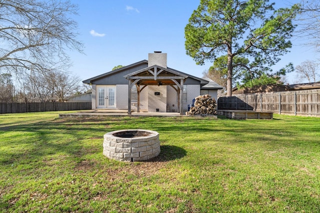 back of property featuring brick siding, an outdoor fire pit, french doors, a chimney, and a fenced backyard