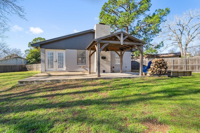 rear view of property with a fenced backyard, a chimney, a gazebo, french doors, and a lawn