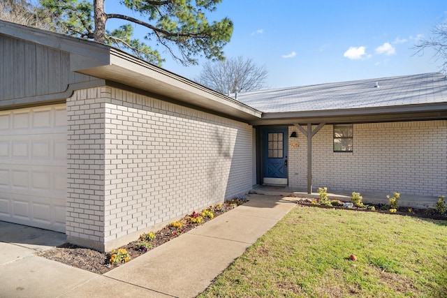 doorway to property featuring a yard, brick siding, and an attached garage