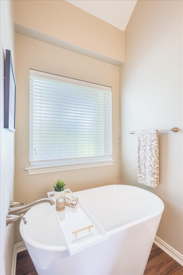 bathroom featuring a freestanding bath, baseboards, and wood finished floors