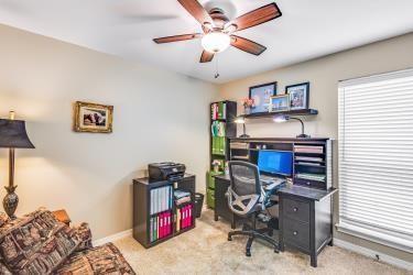 carpeted office space featuring a ceiling fan and baseboards