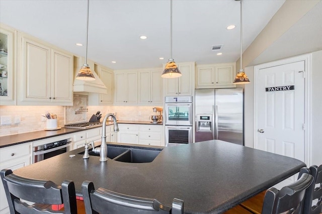 kitchen with visible vents, a sink, dark countertops, cream cabinets, and appliances with stainless steel finishes