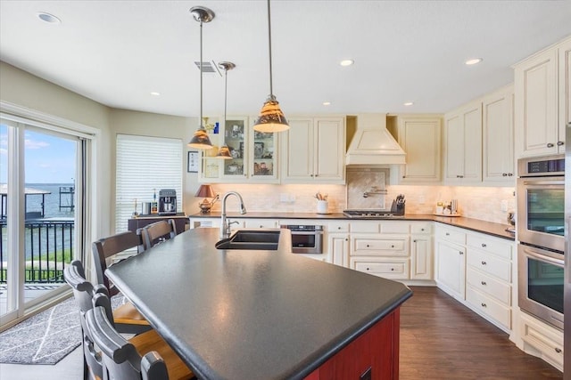 kitchen featuring premium range hood, a sink, dark countertops, appliances with stainless steel finishes, and decorative backsplash