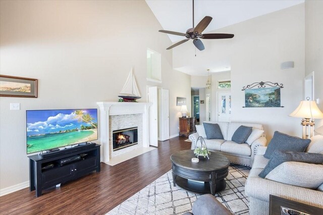 living area with wood finished floors, baseboards, high vaulted ceiling, a fireplace with flush hearth, and ceiling fan