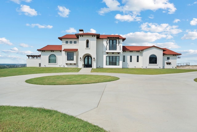 mediterranean / spanish-style house with a front yard, stucco siding, a chimney, and curved driveway