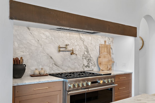 kitchen with light stone countertops, backsplash, and high end range