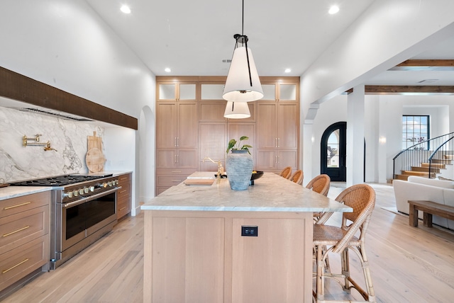 kitchen featuring high end range, a kitchen island with sink, arched walkways, glass insert cabinets, and light wood-type flooring