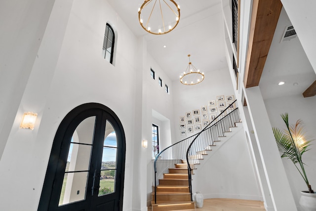 foyer featuring a chandelier, stairs, french doors, wood finished floors, and arched walkways