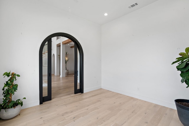 spare room featuring arched walkways, visible vents, baseboards, and light wood-style floors