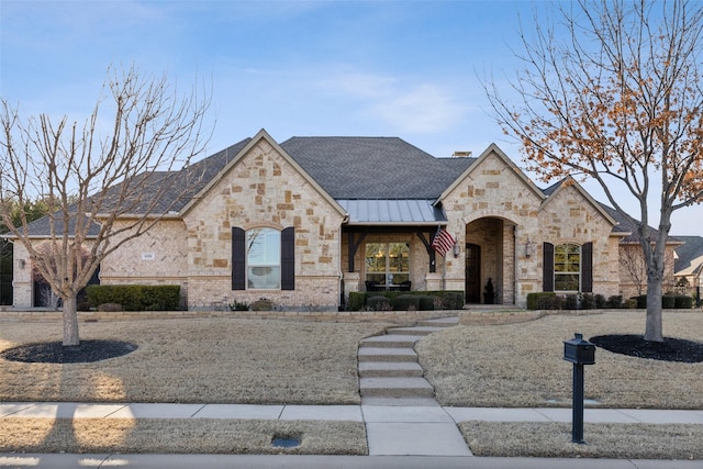 french country style house with a standing seam roof, a shingled roof, metal roof, brick siding, and a chimney