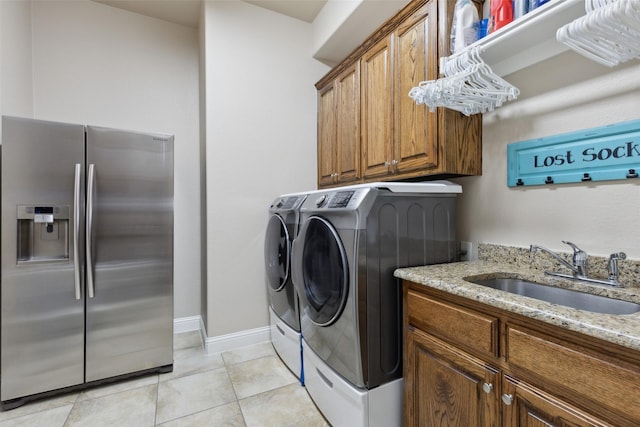 washroom featuring a sink, baseboards, light tile patterned floors, cabinet space, and separate washer and dryer