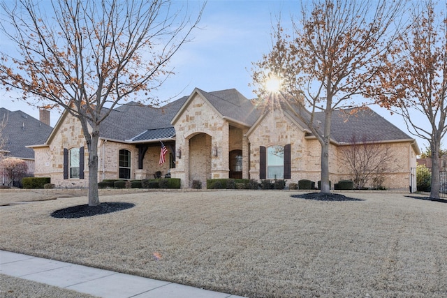 french country inspired facade with a standing seam roof, brick siding, a shingled roof, and metal roof