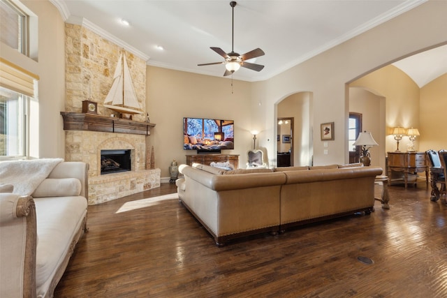 living room with a fireplace, arched walkways, dark wood-style flooring, ceiling fan, and ornamental molding