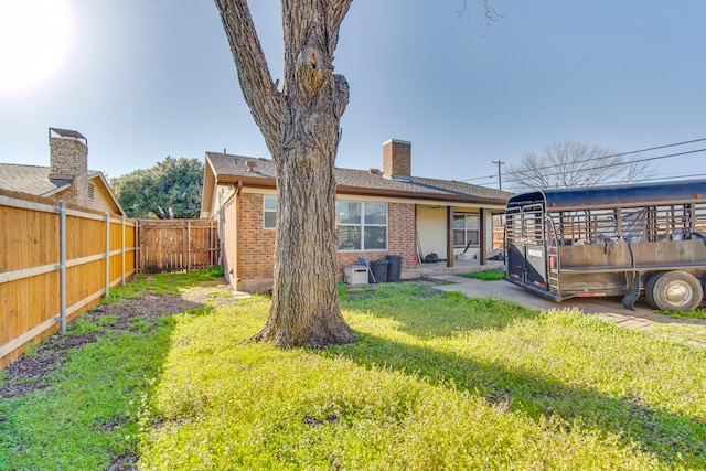 back of house with brick siding, a chimney, a lawn, and fence