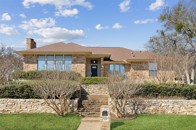 view of front of property featuring brick siding, roof with shingles, and a chimney