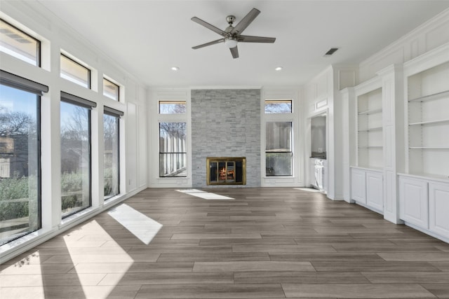 unfurnished living room with visible vents, built in shelves, wood tiled floor, ornamental molding, and a stone fireplace