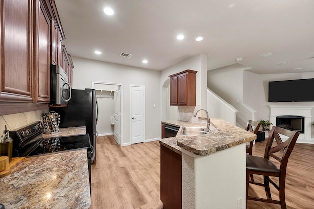 kitchen with a breakfast bar, a peninsula, a fireplace with raised hearth, a sink, and stainless steel microwave