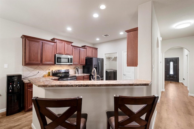 kitchen with visible vents, light wood-style flooring, arched walkways, stainless steel appliances, and a kitchen breakfast bar