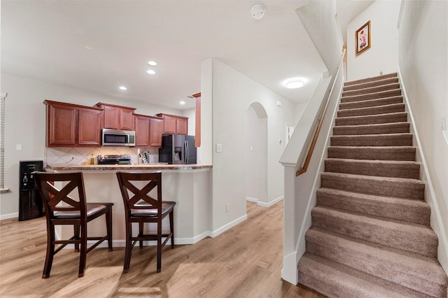 staircase with recessed lighting, wood finished floors, arched walkways, and baseboards