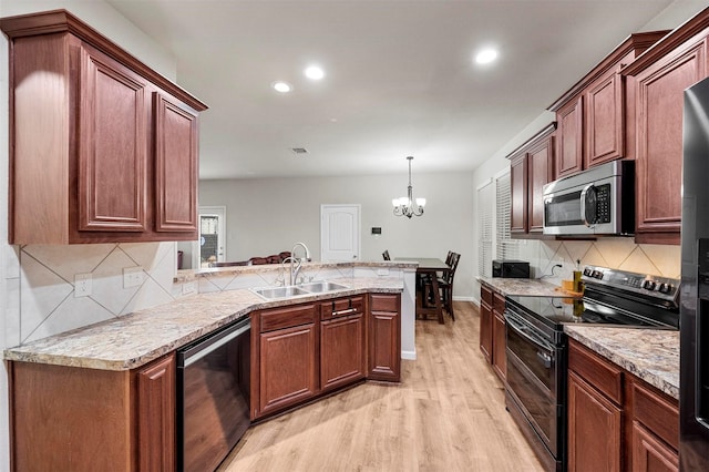 kitchen with a peninsula, range with two ovens, a sink, stainless steel microwave, and light wood-type flooring