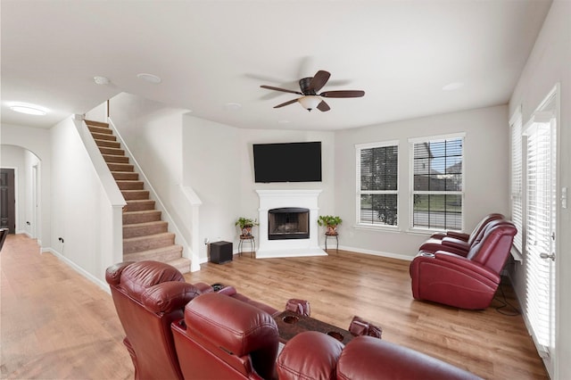 living area featuring arched walkways, a fireplace with raised hearth, stairs, and light wood-type flooring