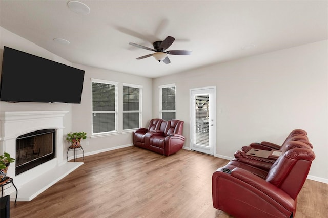 living area with ceiling fan, baseboards, a fireplace with raised hearth, and wood finished floors