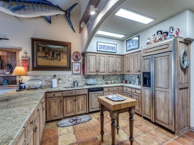 kitchen with paneled fridge, light stone countertops, a sink, tasteful backsplash, and brown cabinets