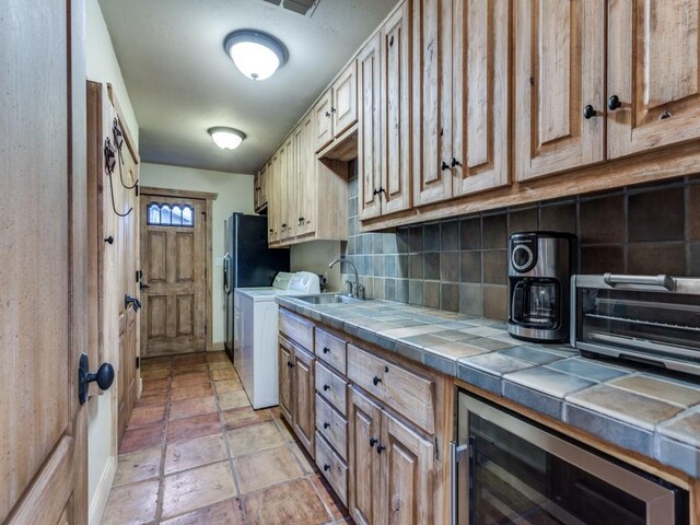 kitchen featuring backsplash, tile counters, beverage cooler, washer / clothes dryer, and a sink