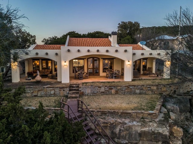 rear view of house with stucco siding, a patio, a chimney, and a tiled roof