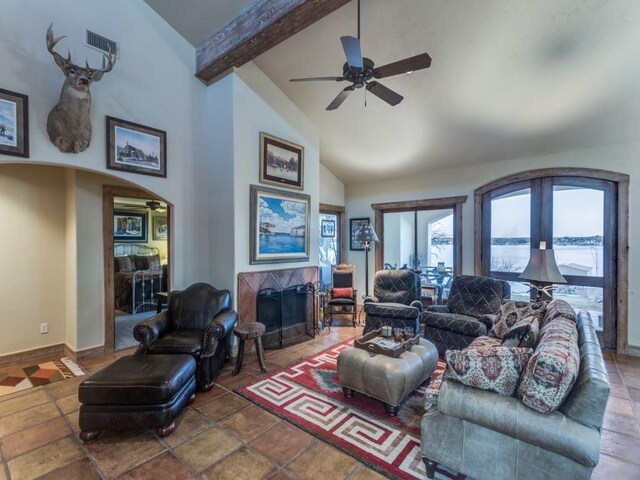 living area featuring ceiling fan, a fireplace with flush hearth, beam ceiling, arched walkways, and high vaulted ceiling