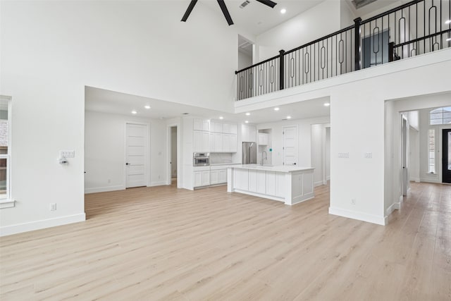 unfurnished living room featuring baseboards, ceiling fan, light wood-style flooring, a high ceiling, and a sink