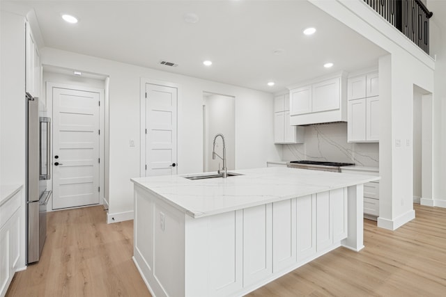 kitchen with a center island with sink, visible vents, a sink, white cabinetry, and light wood-type flooring