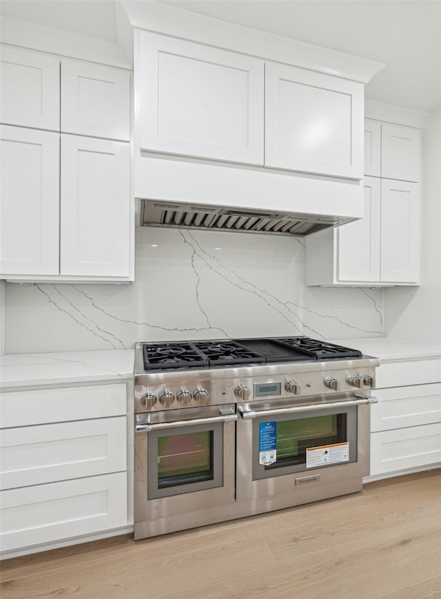 kitchen featuring ventilation hood, light wood-type flooring, range with two ovens, white cabinets, and tasteful backsplash