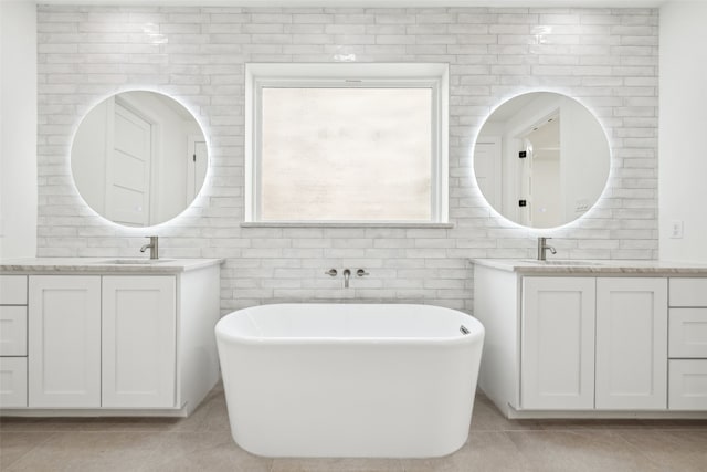 bathroom with tile patterned floors, a soaking tub, two vanities, and a sink