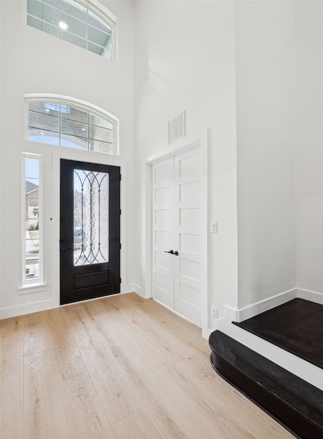 foyer entrance with wood finished floors, visible vents, a towering ceiling, and baseboards