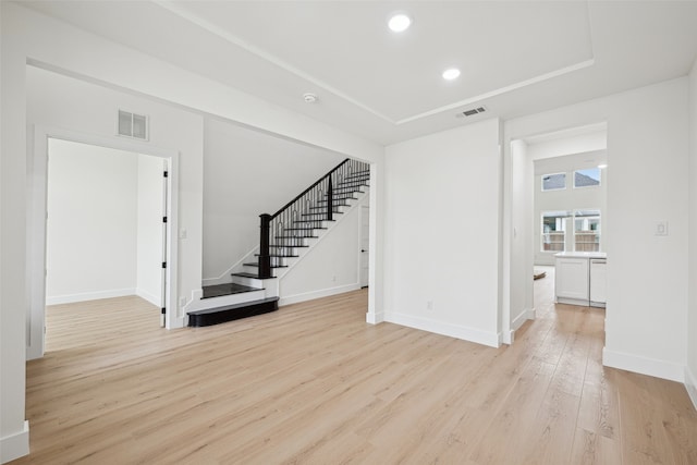 unfurnished living room with stairs, light wood-style floors, visible vents, and baseboards