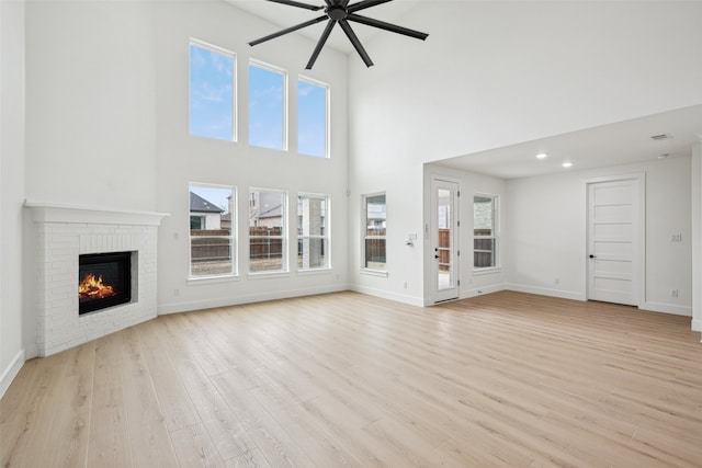 unfurnished living room featuring light wood-style flooring, baseboards, ceiling fan, and a fireplace