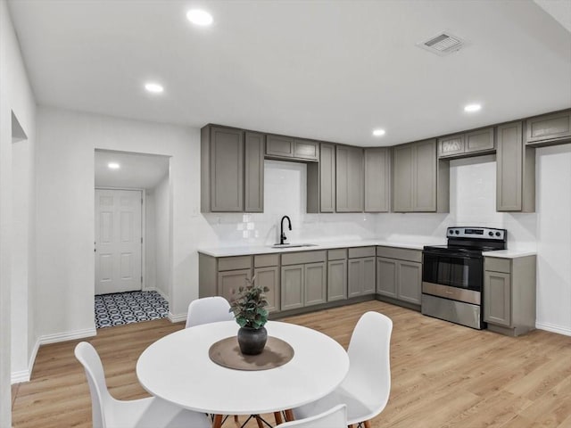 kitchen with visible vents, gray cabinetry, a sink, stainless steel range with electric stovetop, and light wood-type flooring