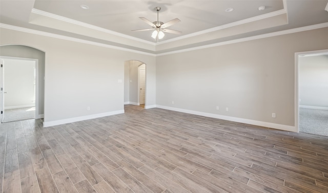 spare room featuring a ceiling fan, a tray ceiling, wood finished floors, and arched walkways