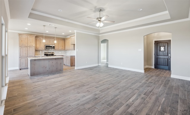 unfurnished living room featuring a tray ceiling, baseboards, arched walkways, and light wood-type flooring