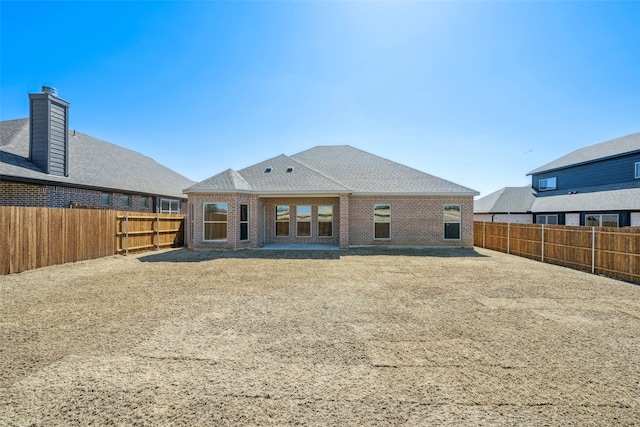 rear view of house with brick siding, a shingled roof, and a fenced backyard