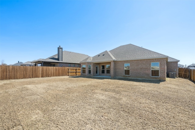 back of property with central AC unit, brick siding, a fenced backyard, and a shingled roof