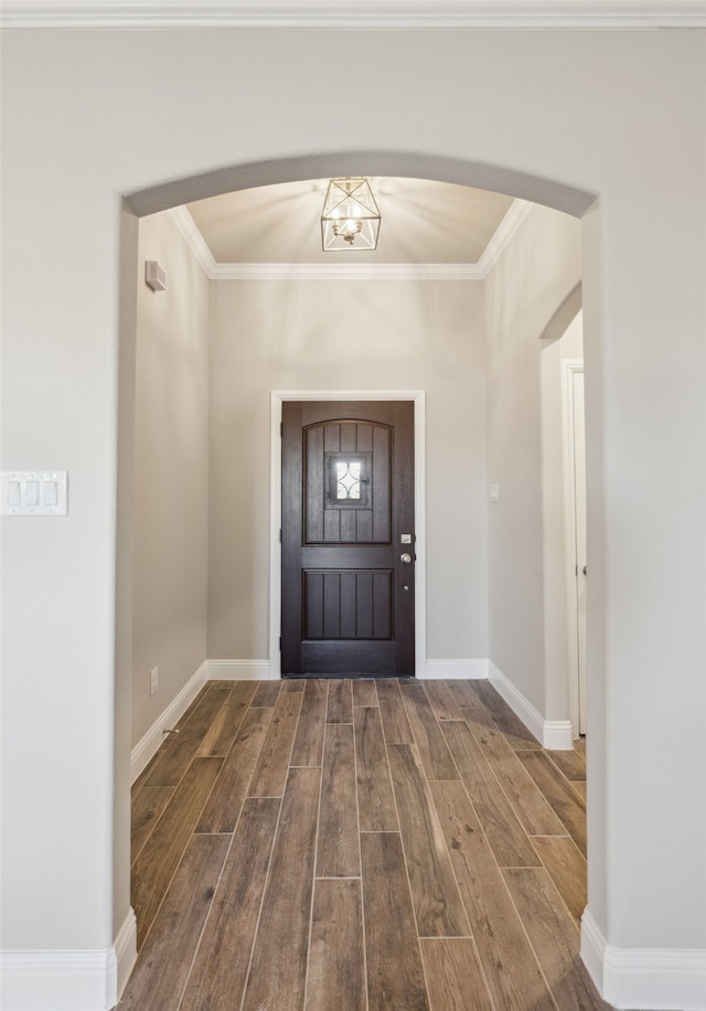 entrance foyer featuring arched walkways, crown molding, baseboards, and wood finished floors