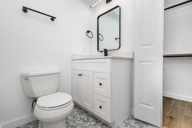 bathroom with vanity, toilet, wood finished floors, and baseboards