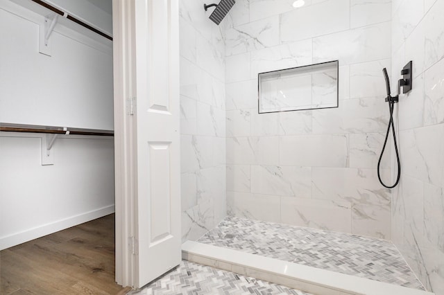 bathroom featuring a tile shower, a spacious closet, baseboards, and wood finished floors