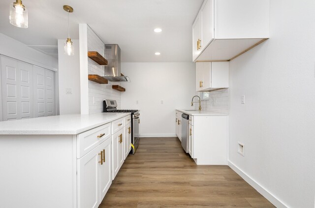 kitchen with open shelves, a sink, light wood-style floors, appliances with stainless steel finishes, and wall chimney range hood