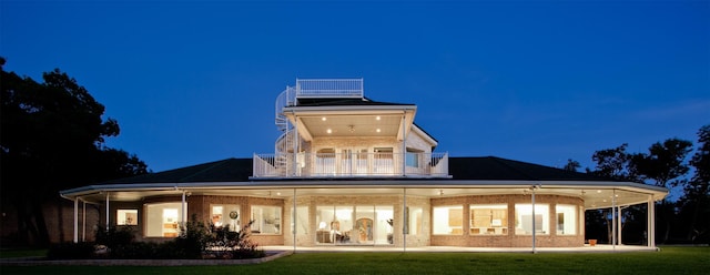 back of house at twilight featuring a balcony, a yard, and brick siding