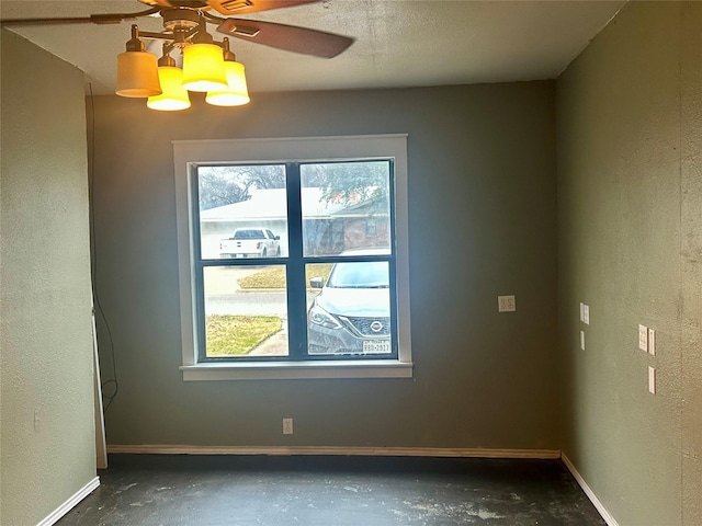 unfurnished room with baseboards, a ceiling fan, unfinished concrete floors, and a textured wall